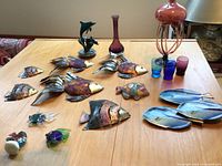 Overview of metal fish wall art, blue fish-shaped dishes, glass fish figurines, vases, and glasses on table.