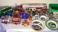 Photo showing multiple kids toys including a large fire rescue truck, Ninja Turtles figures, red helicopter, Lego bin, and plastic play dishes set with farm animal designs.