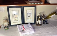 Lighthouse art prints, candle, towel, and sailor statues arranged on table.