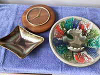 Photo of two ceramic ashtrays and a wooden wall clock on a blue towel background