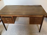 Front view of the desk showing wood grain finish, glass top, and drawers with handles.