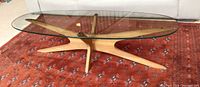 Front perspective of complete coffee table showing oval glass top on teak wood base