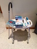 Photo showing shower stool, cane leaning on wall, heating pad box, ice pack and two suction handles on stool seat.