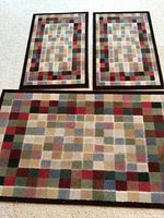 Three multicolored square pattern rugs grouped together on carpeted floor.