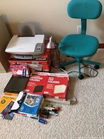 Photo showing Lexmark shredder on top of its box, teal office chair, silver desk lamp, and various office supplies on carpeted floor.