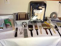 Photo showing the entire painting supplies lot with a collection of brushes, rollers, paint tray, paint can, putty knife and other tools.