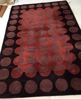 Full view of the rectangular rug, showing the black border with large brown dots and central reddish-brown rectangle with similar dots.