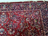 Close-up detail of the floral pattern and border of the red area rug showing intricate multicolor weaving.