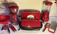 Full view of all red kitchen appliances and utensils including coffee maker, toaster, grill, blender, graters, slicer, can opener, and colander.