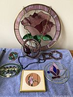 Photo showing the full set of small stained glass hanging pieces including the 16-inch purple rose window, spherical bird piece, and other smaller decorative glass items on a blue cloth.