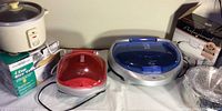 Two George Foreman grills (one small with red lid, one large with blue lid), a Westinghouse 4 cup rice cooker on its box, and a new stainless steel copper bottom soup bowl with lid in box