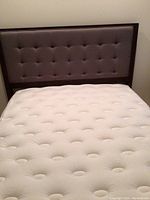 Full view of upholstered headboard in brown fabric with dark wood trim behind a mattress