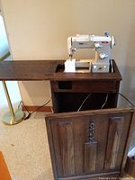 Full view of wooden cabinet with Pfaff sewing machine set inside. Cabinet front panel removed revealing pull-out bench and drawer.