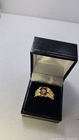Men's gold tone ring with clear stone, displayed in jewelry box.