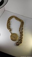 Full view of gold-tone rope chain with round coin pendant lying flat