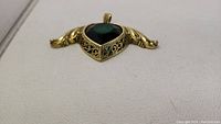 Pendant with large green heart-shaped faceted stone set in gold-toned filigree, showing side detail of metalwork