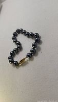 Full view of the faux pearl bracelet laid flat, showing the round black beads and gold clasp.