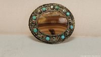Full view of oval brooch with central banded agate and turquoise stones in silver filigree frame.