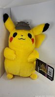 Yellow Detective Pikachu plush with hat and original tags visible inside white box.
