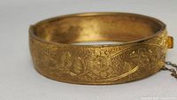 Close-up front view of the gold tone Victorian cuff showing detailed hand engraved floral pattern on the outer surface with leaves and flowers.