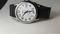 Front view of Timex Indiglo watch face showing white dial with date window at 3 o'clock and black nylon strap.