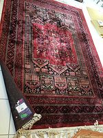 Full view of the red and black patterned carpet laid flat showing its overall design and condition.