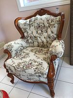 Front view of vintage carved wood frame chair with cream background floral brocade upholstery and tufted backrest