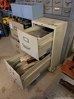 Front and top view of an off-white metal two drawer filing cabinet with both drawers open showing tools inside.