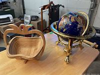 Photo showing both the decorative globe on brass stand and the wooden apple-shaped collapsible basket on a table in garage setting.