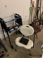 Photo showing Hugo folding walker, white shower chair with black device on seat, some garden tools in background