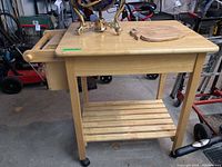 Front and side angle of wood rolling kitchen cart showing drawer, slatted lower shelf, side handle, and storage box.