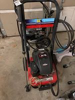Front angle of BE power washer showing Briggs & Stratton engine cover marked 4.75 HP, hose, spray wand and red frame.