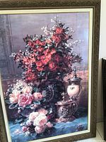 Front view of large floral print with red, pink, and white flowers along with ornamental vessels on a blue surface, set against a muted background.