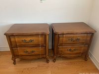 Front view of two vintage solid wood side tables with ornate metal handles on drawers.