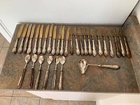 Overview of 12 knives and 12 forks laid out on countertop