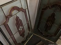 Two matching stained glass panels leaning against a wall, showing overall design and the crack on the bottom of one panel.