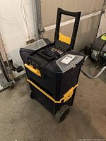 Full view of the closed tool box showing black body with yellow latches, wheels, and retractable handle in garage.
