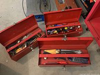 Three red metal toolboxes with lids open, showing an assortment of hand tools and hardware inside