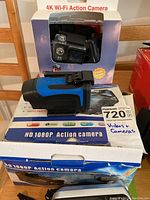 Photo showing 4K Wi-Fi action camera in packaging and HD 1080P action camera with blue and black body on box