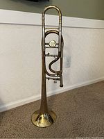 Full view of trombone upright against wall showing overall shape and condition