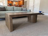 Angled left view of table showing rectangular top, cylindrical base, panel base, and wood grain finish.