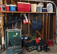 Overview of lot showing coolers and buckets on shelf, camp stove cases and lanterns below