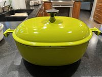 Front view of oval lime green Dutch oven with lid on black countertop, showing Enzo Mari design and chips on rim.