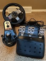 Overall shot showing Logitech steering wheel, pedal set, and gear shifter placed on carpeted floor with cables connected.