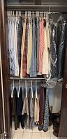 Closet view of men's dress shirts hanging on top rack showing multiple checkered and solid color dress shirts.