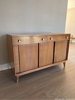 Front side view of wooden credenza with three drawers and sliding doors.