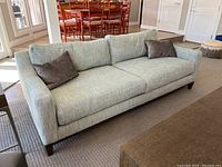 Front view of light turquoise Bassett sofa with two dark gray pillows, placed on carpeted floor in living room.
