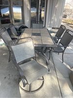 View of patio dining table with six mesh chairs, including swivel chairs, on concrete patio under covered area