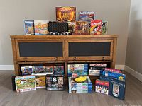 Overview of puzzles and board games stacked on and in a wooden cabinet. Includes various classic board games on top and multiple puzzle boxes below.