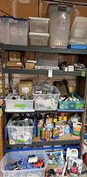 Full view of metal shelving rack filled with labeled plastic bins containing various small hardware, screws, cleaning products, and cans of paint or finishes